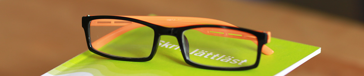Glasögon som ligger på ett häfte med texten Skriv lättläst.